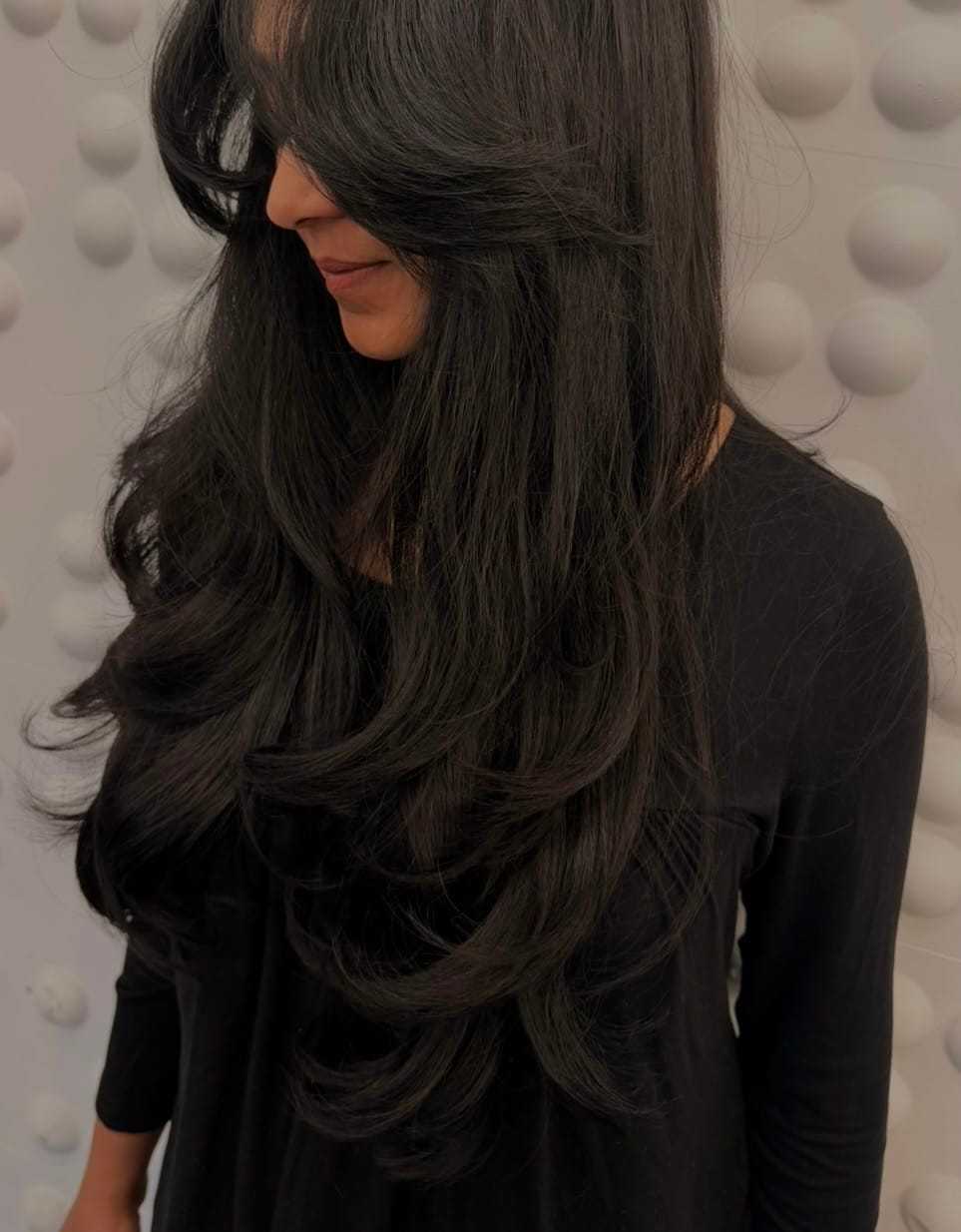 Long, wavy dark hair styled in layers against a textured white background.