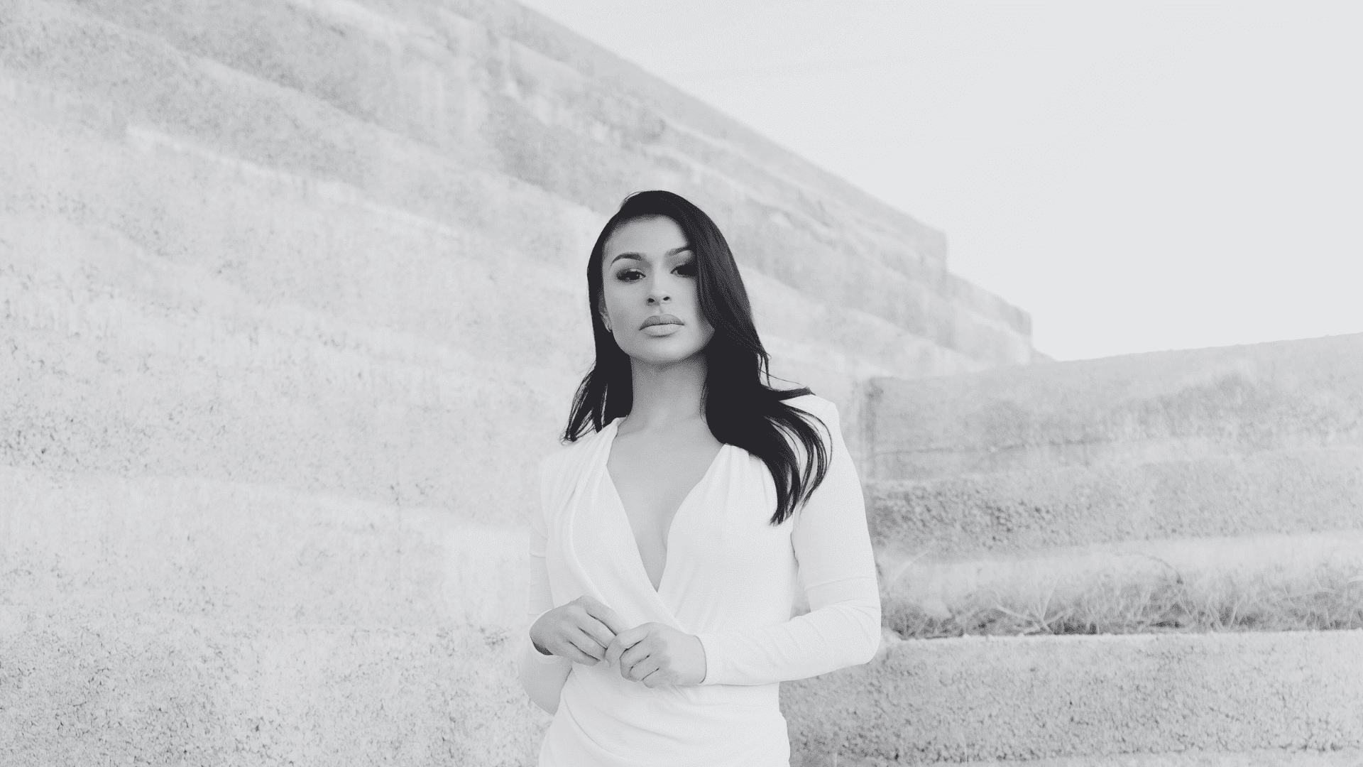 Woman in white dress standing by textured concrete steps. Monochrome photo.
