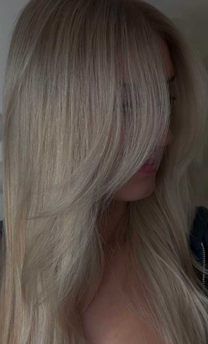 Blonde woman with long hair partially covering her face, wearing a dark top.