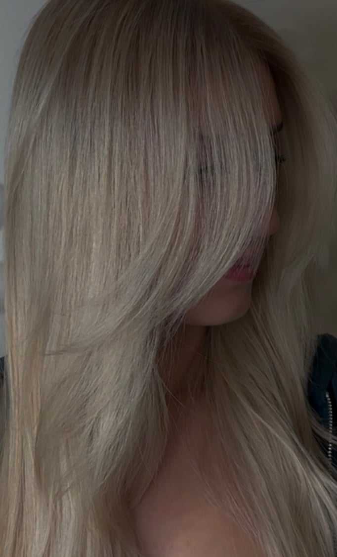 Blonde woman with long hair partially covering her face, wearing a dark top.