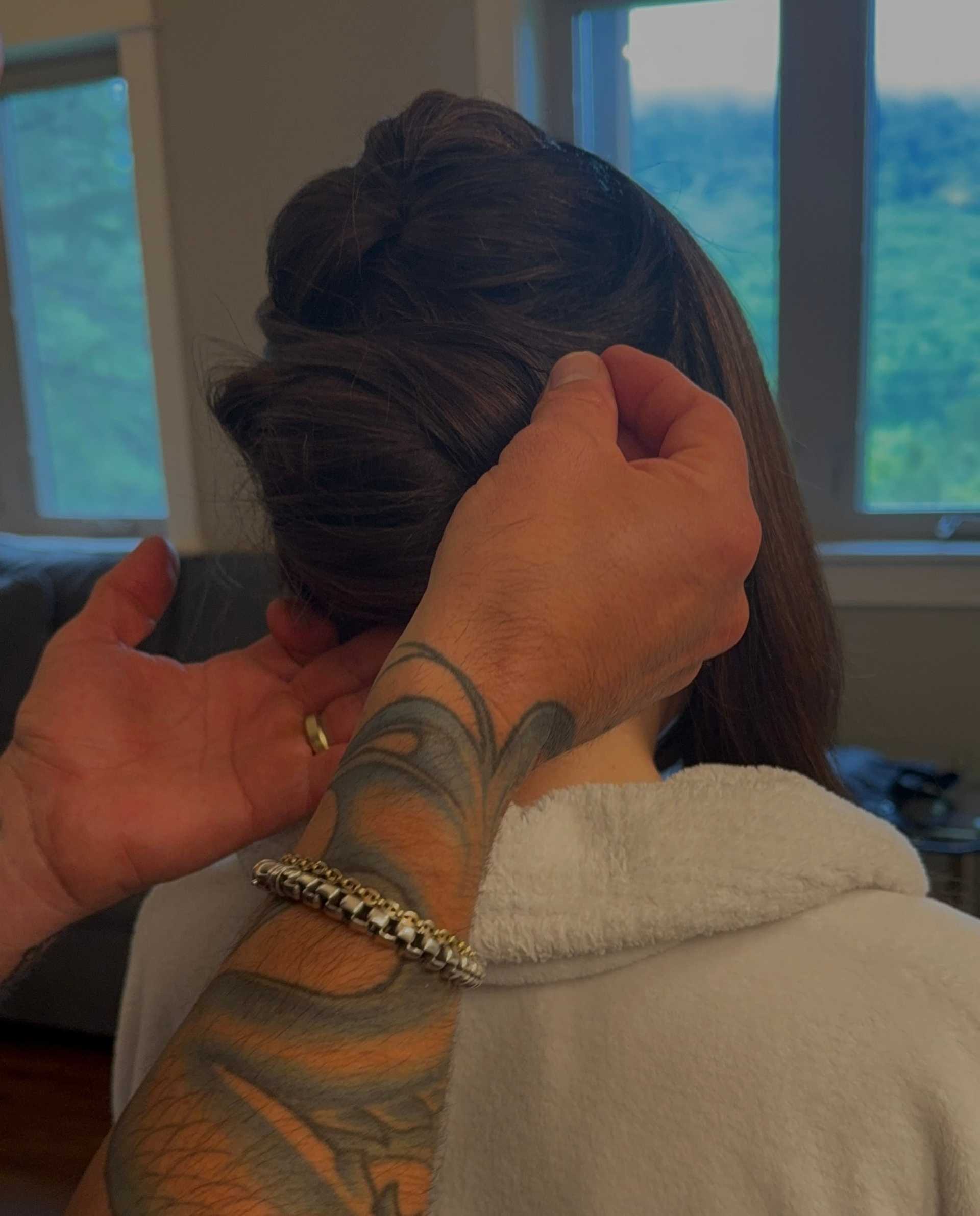 Man styling a woman's hair in a cozy room with scenic window view.